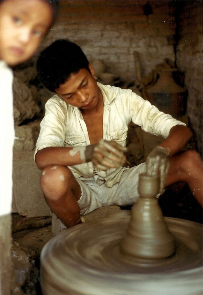 A photo of a young boy churning out clay cups for yoghurt on a foot-powered potter's wheel.