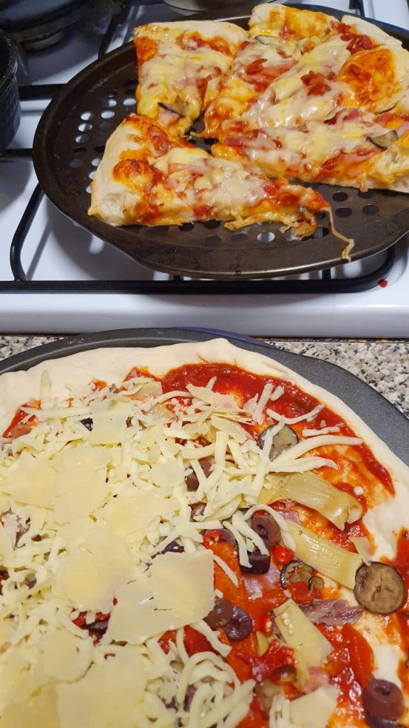 A photo showcasing a cooked home-made gourmet pizza next to an uncooked pizza.