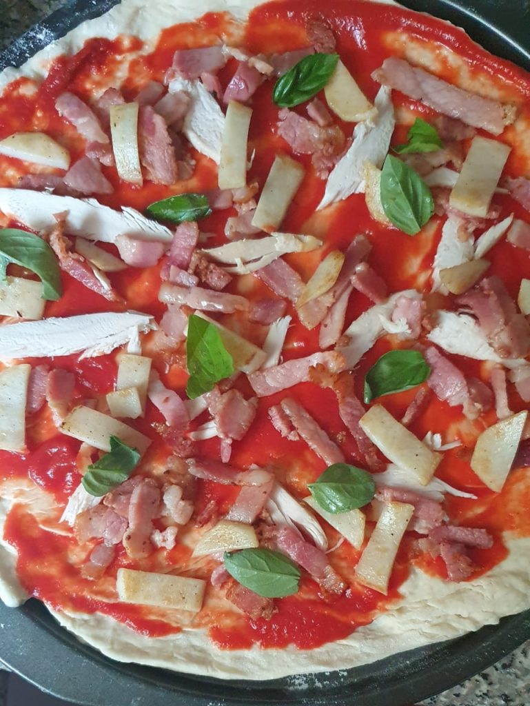 A photo of a home-made gourmet pizza with chicken, bacon, potato, basil toppings - ready to cook.